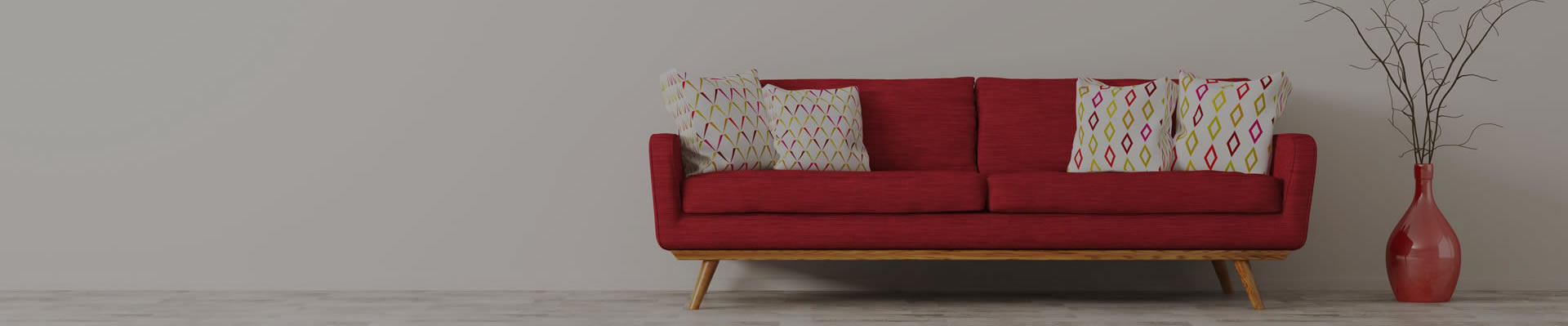 Crvena sofa sa belim jastucima pored koje je crvena vaza